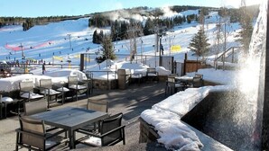 Un espace extérieur aménagé avec des tables et des chaises, offrant une vue sur une piste de ski enneigée, avec un télésiège et des skieurs.