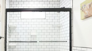 Une salle de bain avec des carreaux de métro blancs, une baignoire noire, des toilettes et un lavabo doté d’un plan de toilette beige.
