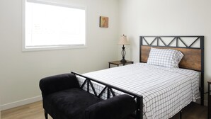 Une chambre à coucher avec un lit, une chaise, une table de chevet, une lampe et une fenêtre.