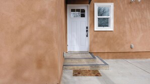 Une entrée de maison avec une porte blanche, une petite fenêtre et une allée en béton.