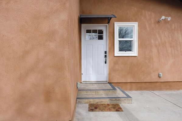 A house entrance with a white door, a small window, and a concrete driveway.
