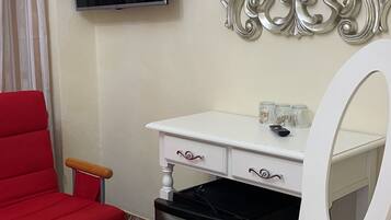 A room with a red chair, a white desk, a black trash bin, a television, and a mirror with an ornate frame.