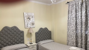 A hotel room with two beds, a nightstand, a lamp, a floral painting, and a curtain. - Hostal Lojo (Conil de la Frontera)