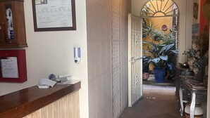A hallway with a reception desk, a framed document on the wall, and a door leading to a room with plants. - Hostal Lojo (Conil de la Frontera)