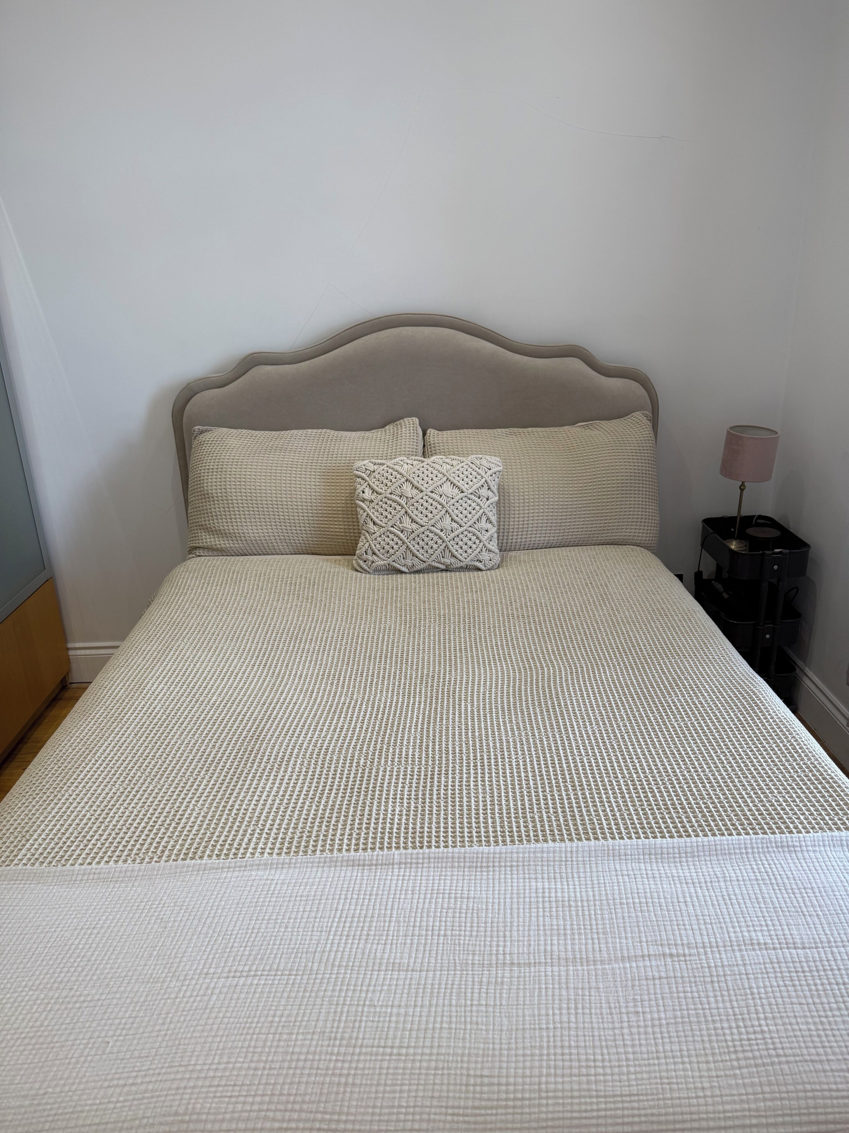 A bed with a patterned bedspread, two pillows, a headboard, and a bedside table with a lamp.
