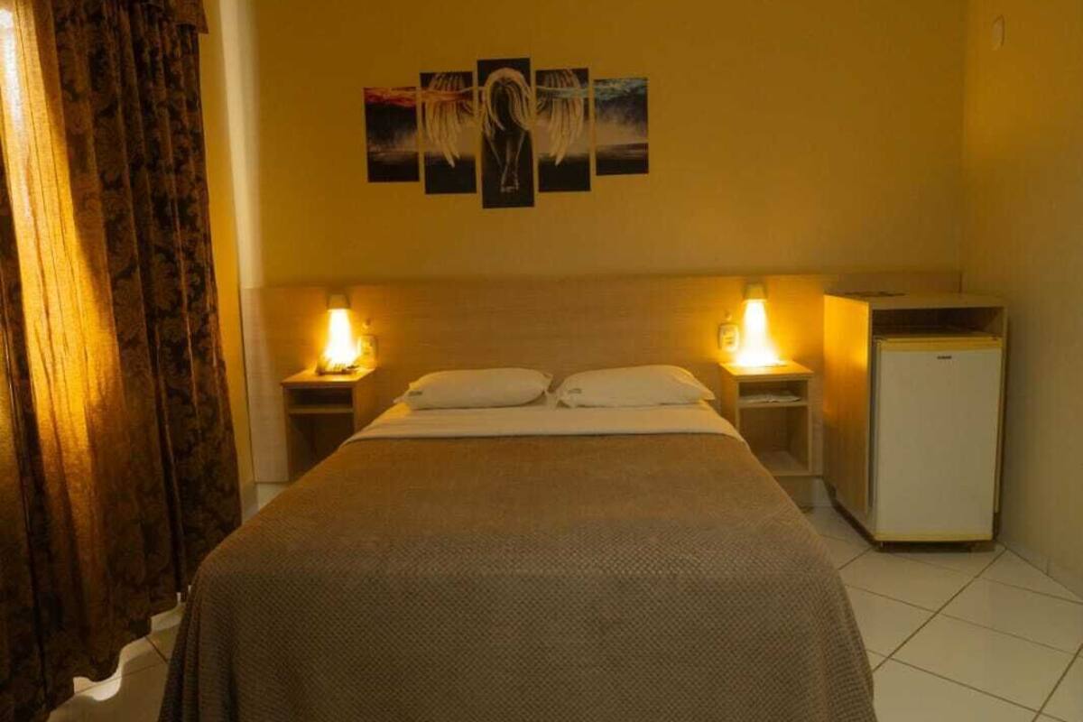 A hotel room with a bed, two bedside tables with lamps, a small refrigerator, and a wall with three framed pictures.