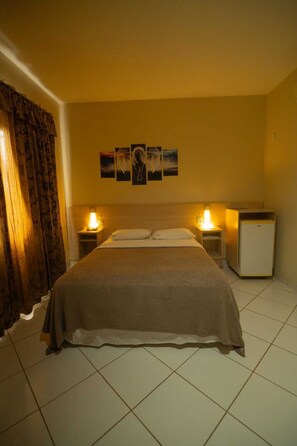 A hotel room with a bed, two bedside tables with lamps, a small refrigerator, and a wall with three framed pictures. - VITORIA PALACE HOTEL (Sinop)