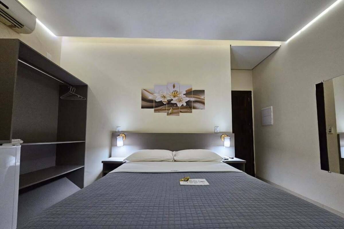 A hotel room with a bed, bedside tables, a wardrobe, and a wall-mounted artwork.
