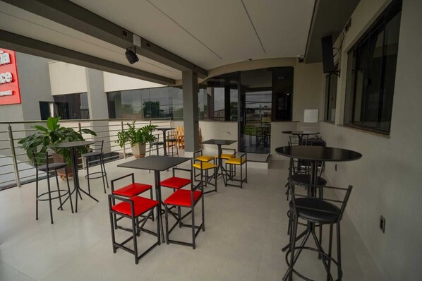 A modern outdoor seating area with tables and chairs, potted plants, and large windows offering views of the surroundings. - VITORIA PALACE HOTEL (Sinop)