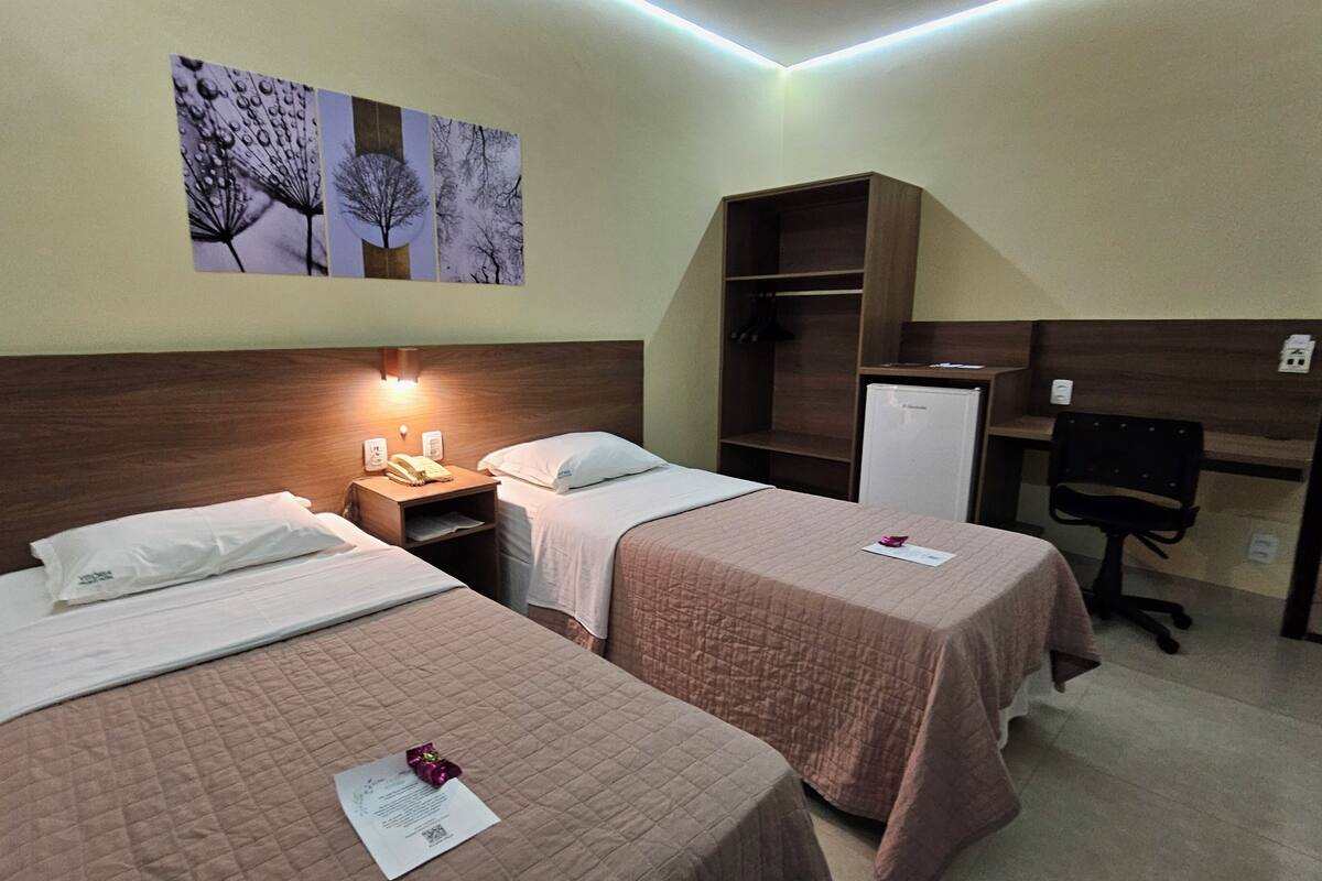 A hotel room with two beds, a desk, a chair, a wardrobe, and a refrigerator.
