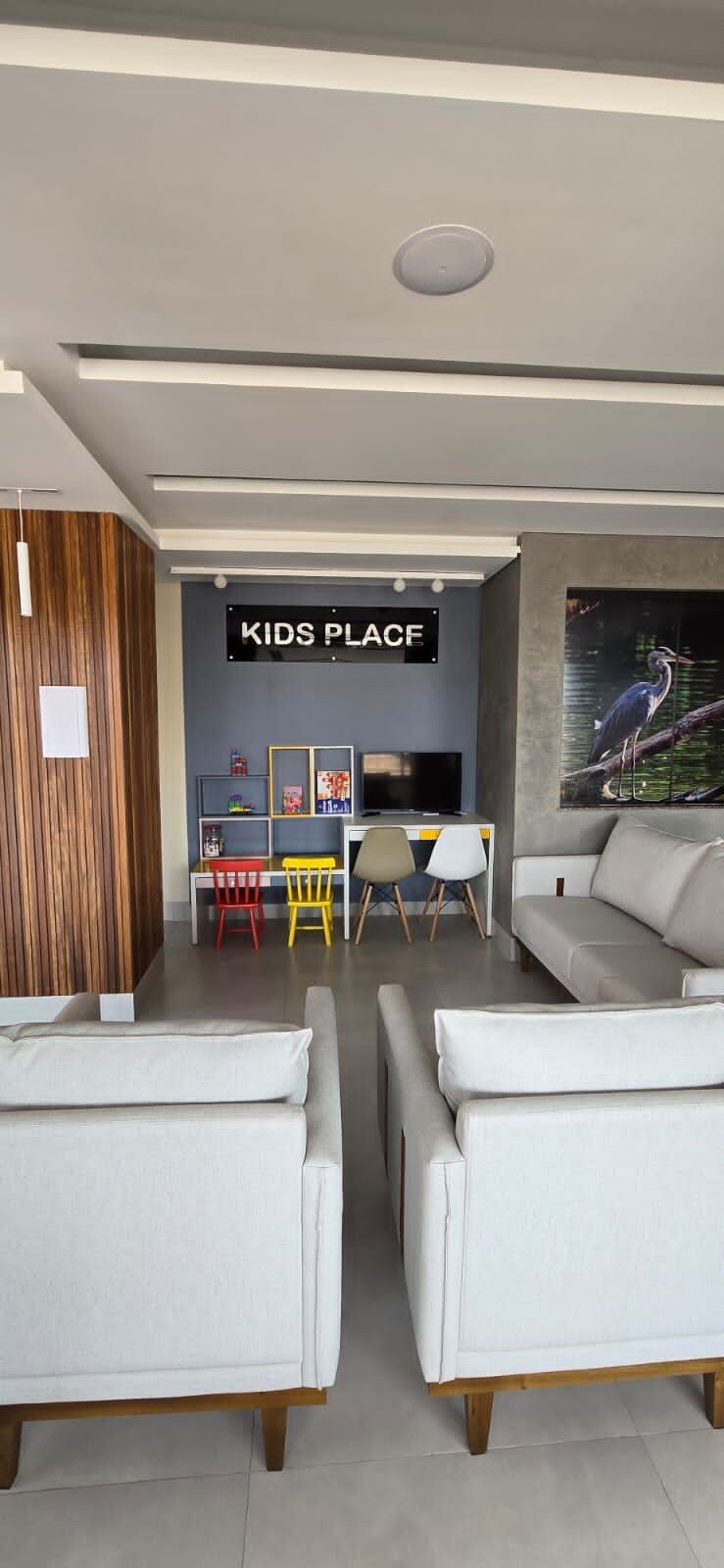 A modern living room with a sofa, a TV, and a children's play area with a sign reading 'KIDS PLACE'.