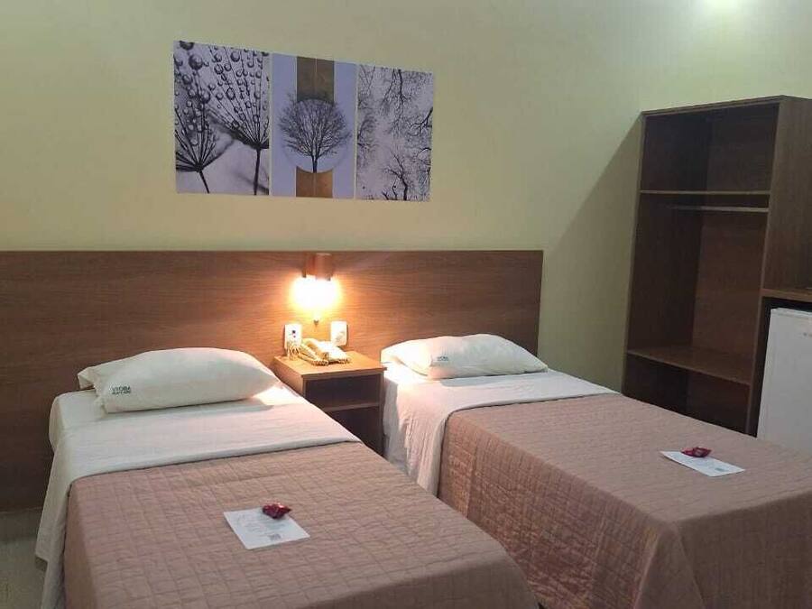 Una habitación de hotel con dos camas individuales, una mesita de noche con lámpara, un armario de madera y un refrigerador pequeño.