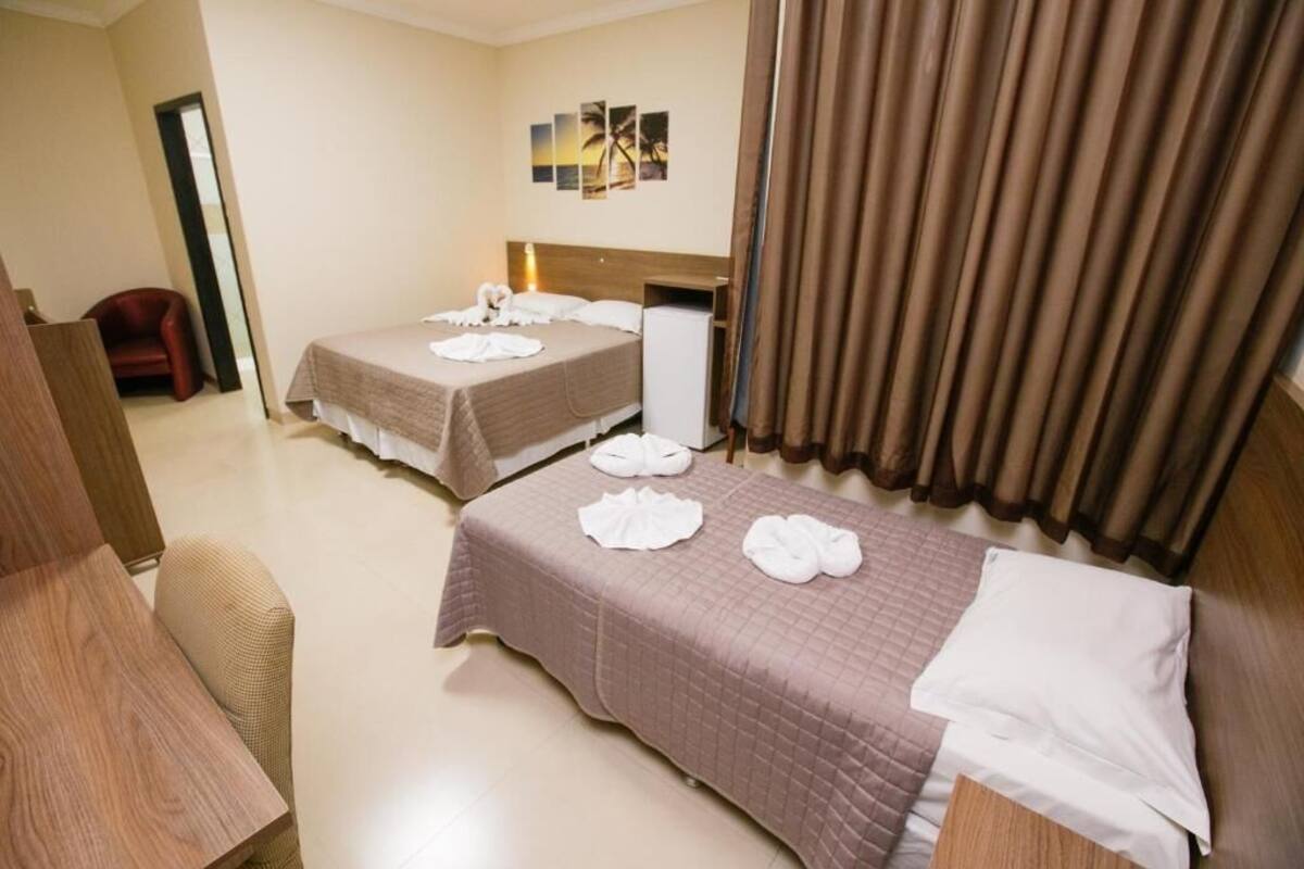 A hotel room with two beds, a wooden desk, a chair, and a small table.