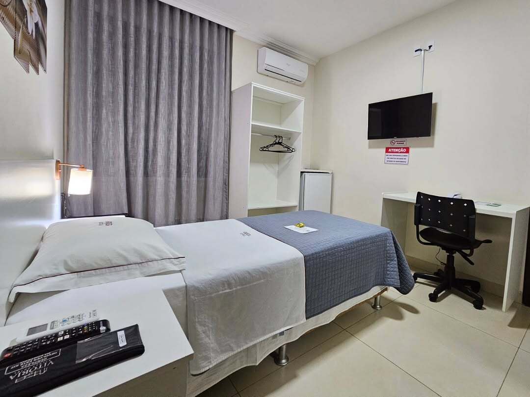 A hotel room with a bed, a desk, a chair, a TV, and a wardrobe.