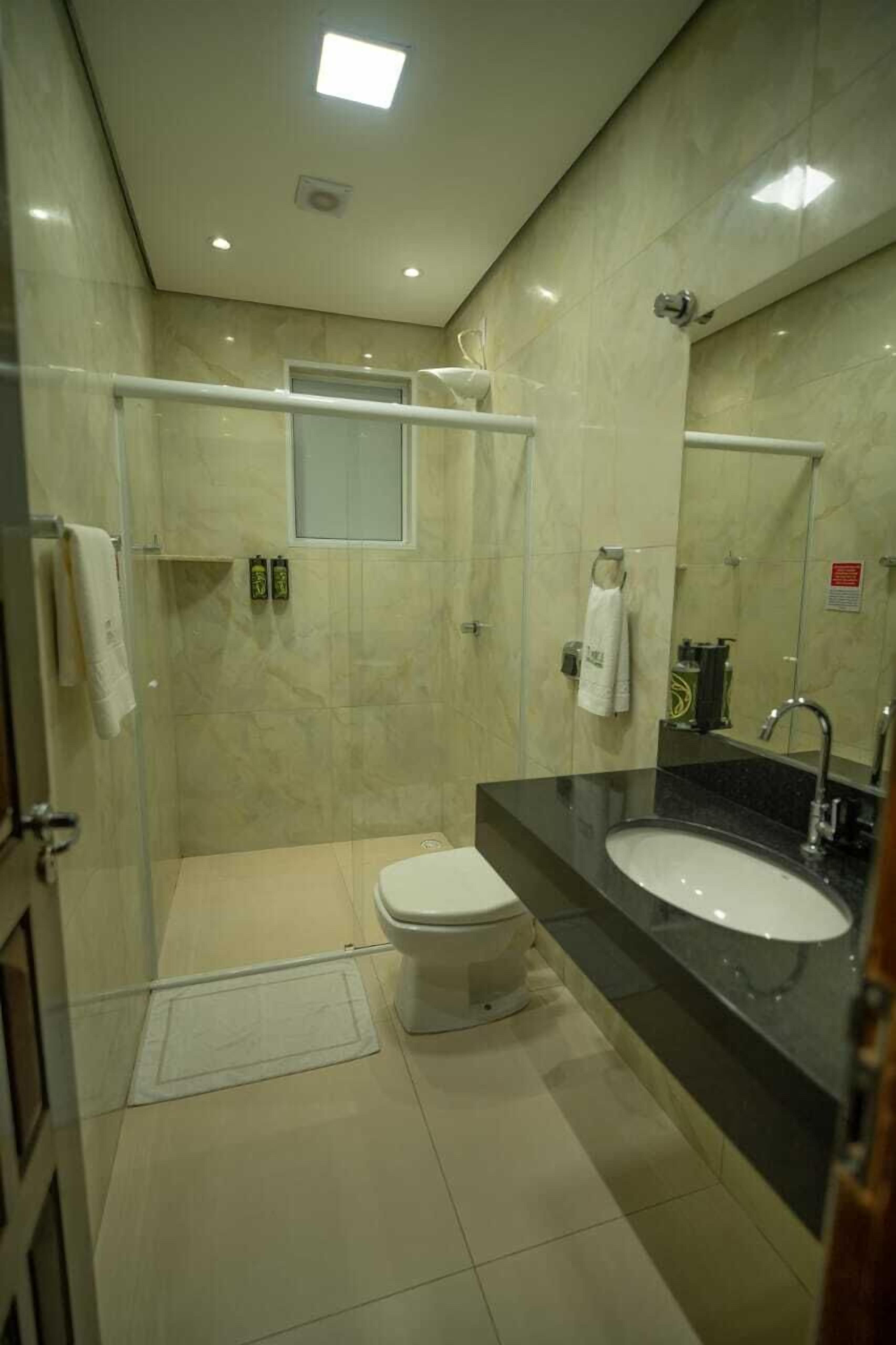 Un baño moderno con cabina de ducha de vidrio, inodoro, lavamanos y un espejo grande.