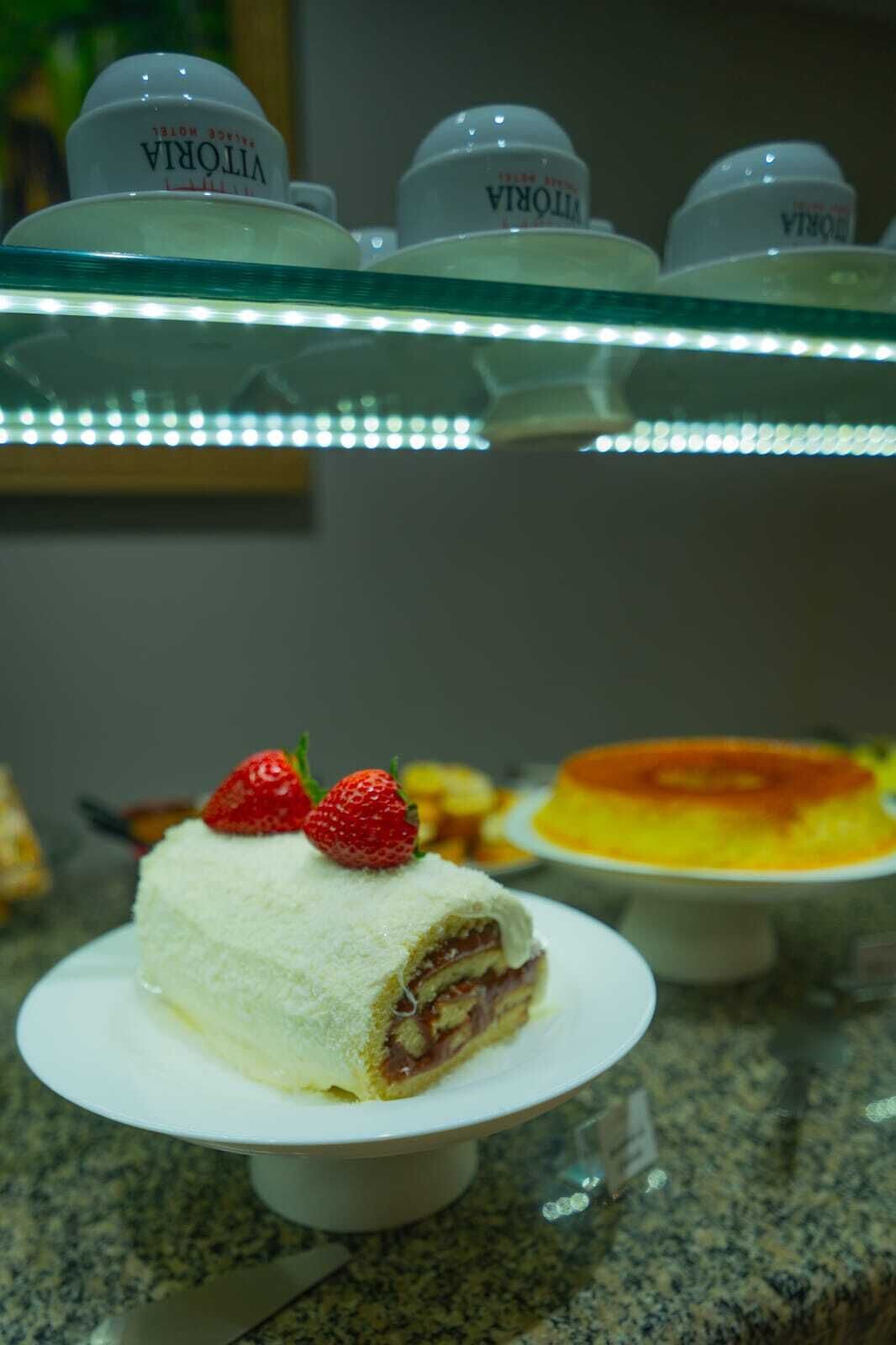 A dessert display with a cake topped with strawberries, under a glass case with LED lights.