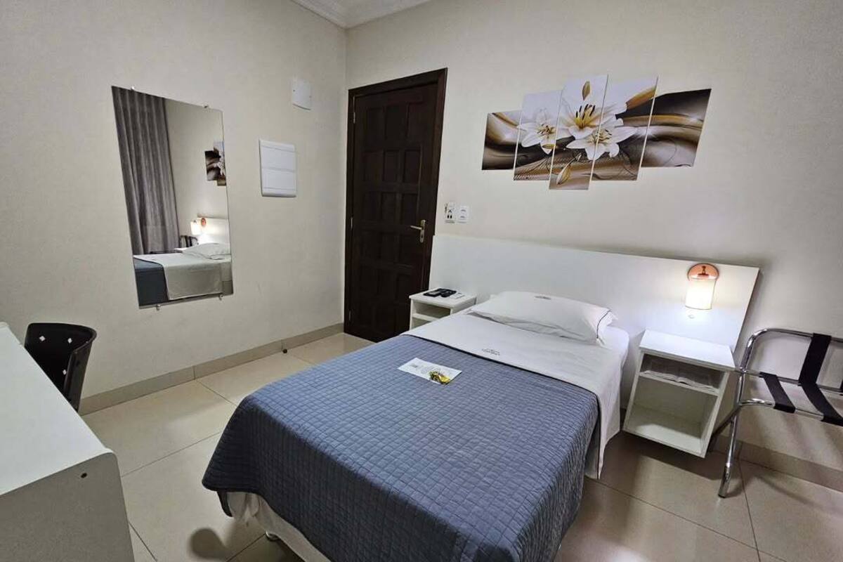 A hotel room with a bed, bedside table, lamp, and a mirror.