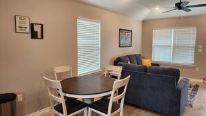 A dining area with a round table and chairs, a gray sofa, and a ceiling fan. - Country Cabin Getaway (Lometa)