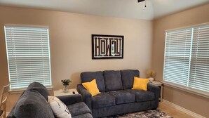 A living room with a gray sofa and armchair, a black and white rug, and a wall-mounted artwork. - Country Cabin Getaway (Lometa)