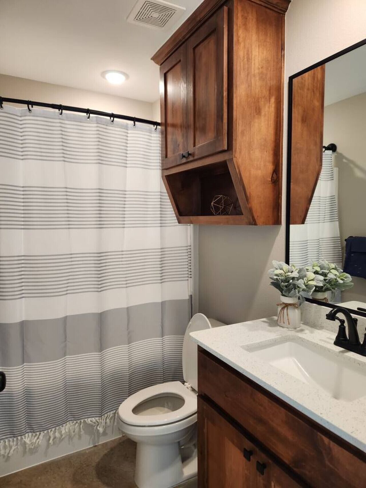 A bathroom with a striped shower curtain, a white toilet, wooden cabinets, and a mirror above the sink.