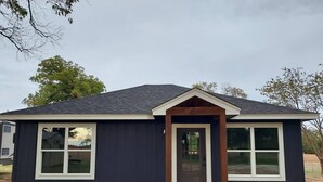 A single-story house with a dark exterior, a front door, and two windows on the side. - Country Cabin Getaway (Lometa)