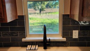 A kitchen with a window, a sink, and a wooden cutting board. - Country Cabin Getaway (Lometa)