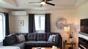 Una sala de estar con un sofá seccional, una mesa de centro de madera, un reloj de pared, un televisor y una chimenea.