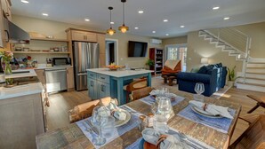 Una cocina moderna con una isla central, comedor con una mesa para cuatro y sala de estar con un sofá y una escalera.