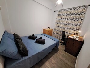 Un dormitori petit i ordenat, amb un llit, una taula de treball i una cadira.