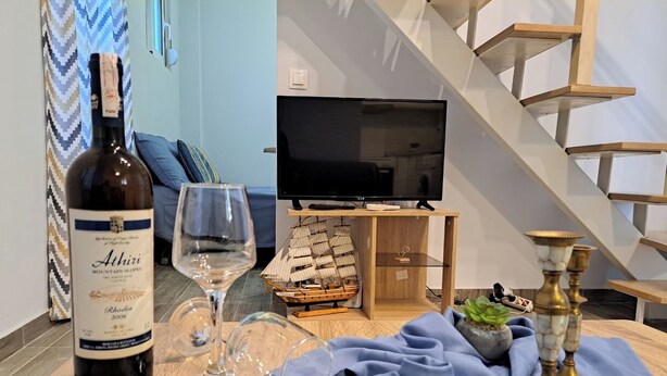 Ein Zimmer mit Holztisch, einer Weinflasche, einem Glas, einem Schiffmodell und einem Fernseher.