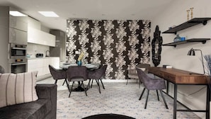 Eine moderne Küche mit weißen Schränken, ein Essbereich mit floralem Wandpapier und ein Arbeitsbereich mit Schreibtisch und Regalen.