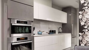 Eine moderne Küche mit eingebauten Backöfen und einer Mikrowelle, weißen Schränken und floralem Wandpapier auf der rechten Seite.