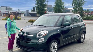 Un parcheggio con un'auto verde scuro e una persona in piedi accanto.