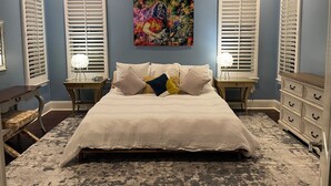 A bedroom with a large bed, two nightstands, a ceiling fan, and a colorful painting on the wall.