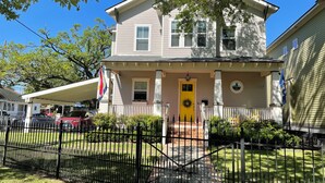 A two-story house with a yellow front door, a porch with a white railing, and a brick pathway leading to the entrance.