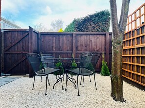 Un patio con una mesa y sillas, rodeado por una cerca de madera y un árbol.