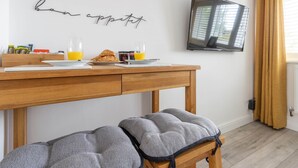 A breakfast setup with croissants and orange juice on a wooden table, a TV mounted on the wall, and a bench with cushions. - Stylish Cheshire House (Winsford)