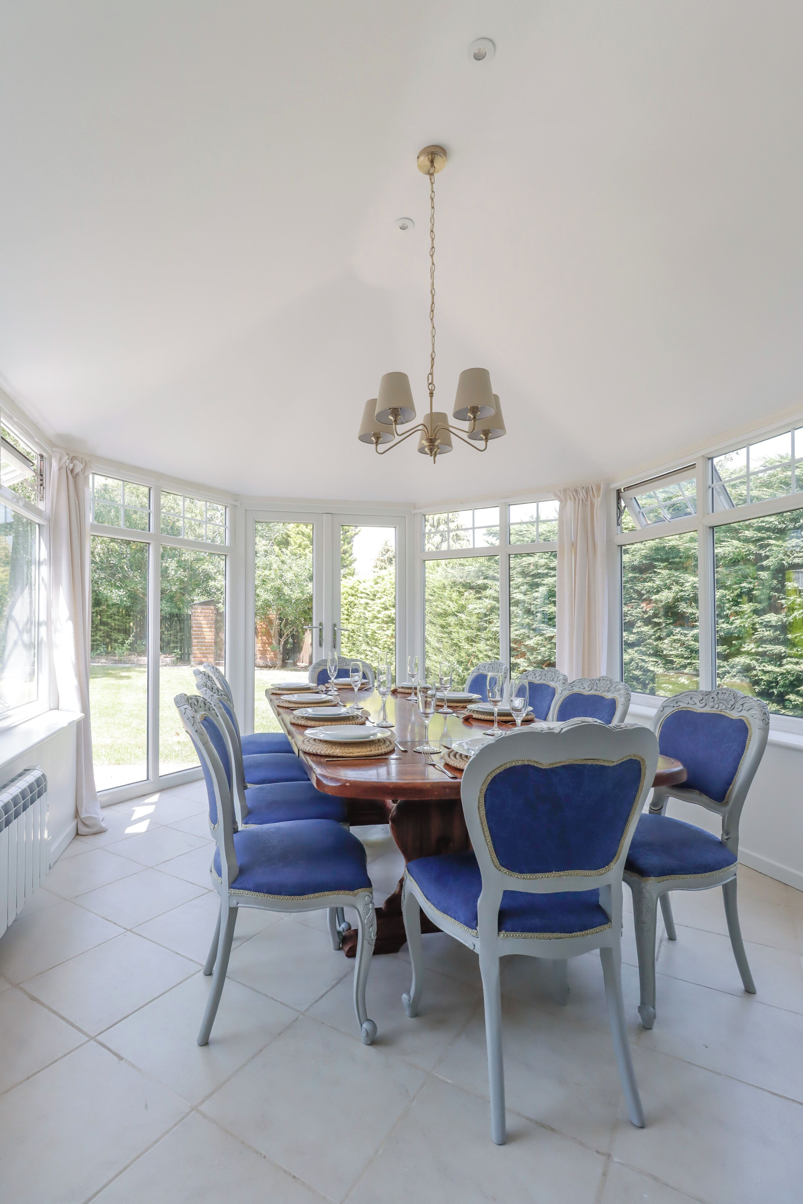A dining room with a large table set for six, surrounded by six chairs with blue upholstery.