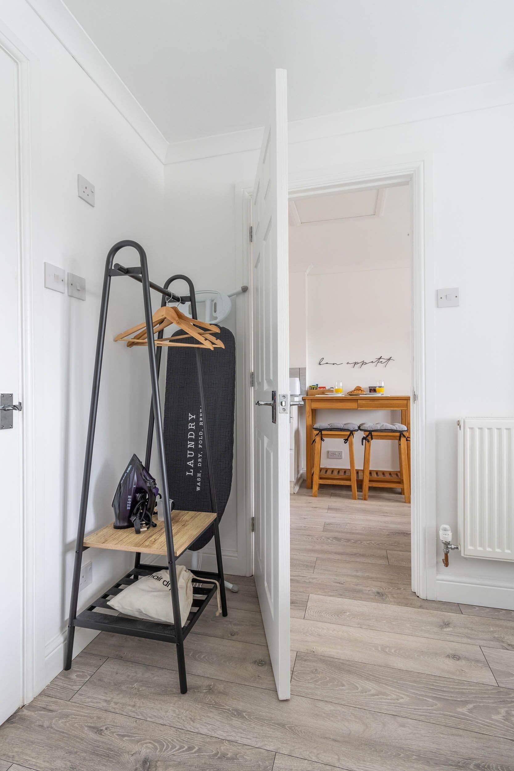 A hallway with a black laundry stand, a wooden table with chairs, and a sign on the wall.
