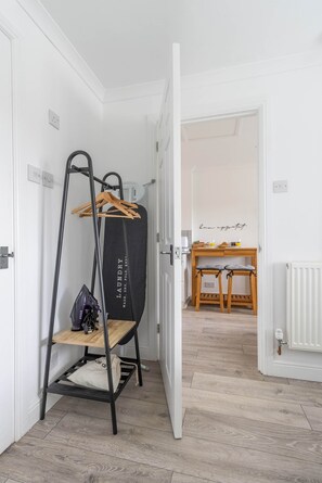 Un couloir avec un étendoir noir, une table en bois avec des chaises et un panneau accroché au mur.