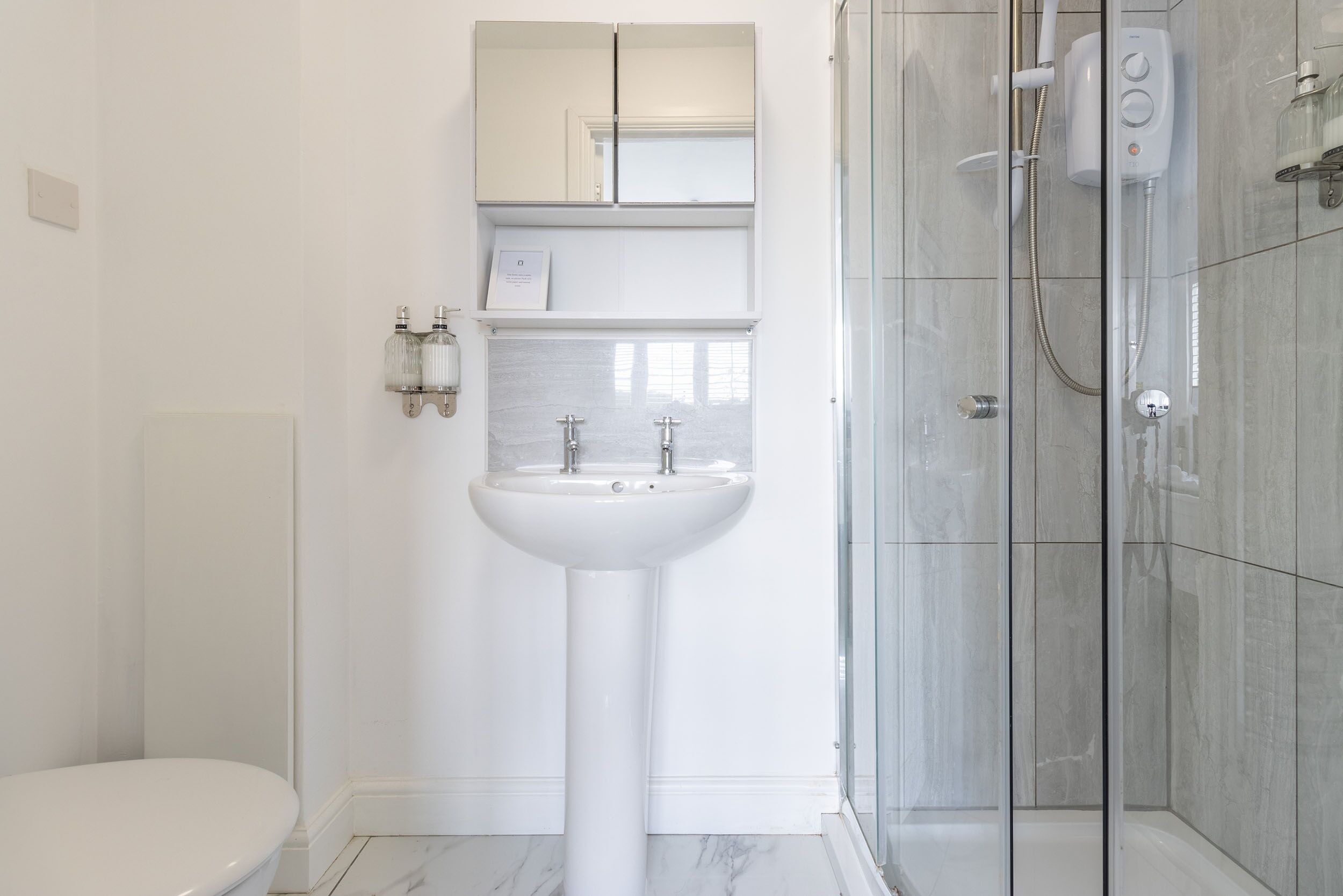 A modern bathroom with a pedestal sink, a glass shower enclosure, and a toilet.
