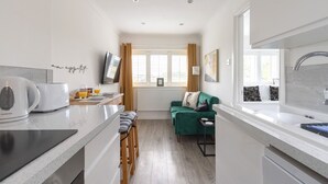 A modern kitchen with a built-in stove, bar stools, a green sofa, and a large window with curtains. - Stylish Cheshire House (Winsford)