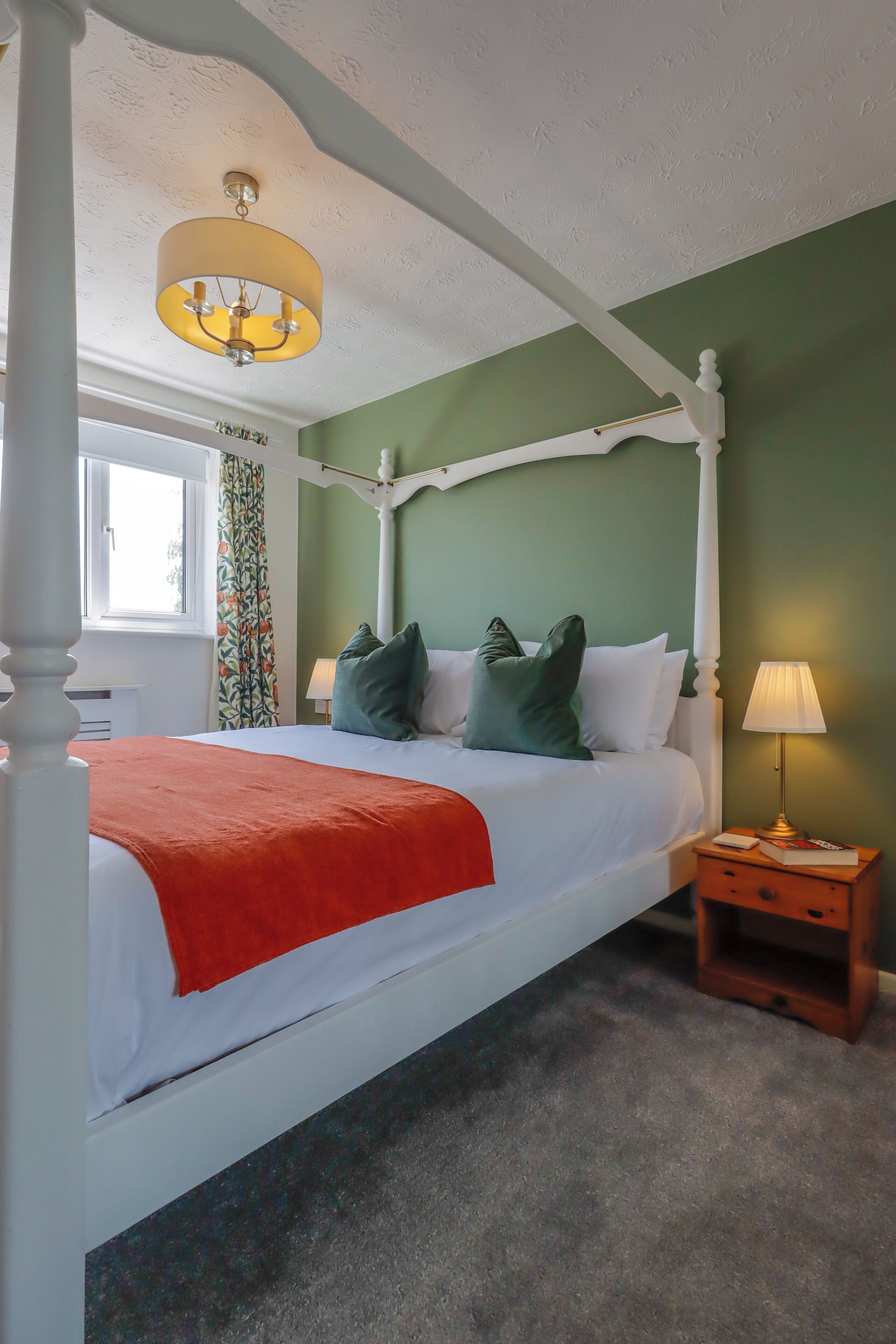 A four-poster bed with a white canopy, green walls, and a window with curtains.