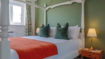 A four-poster bed with a white canopy, green walls, and a window with curtains.