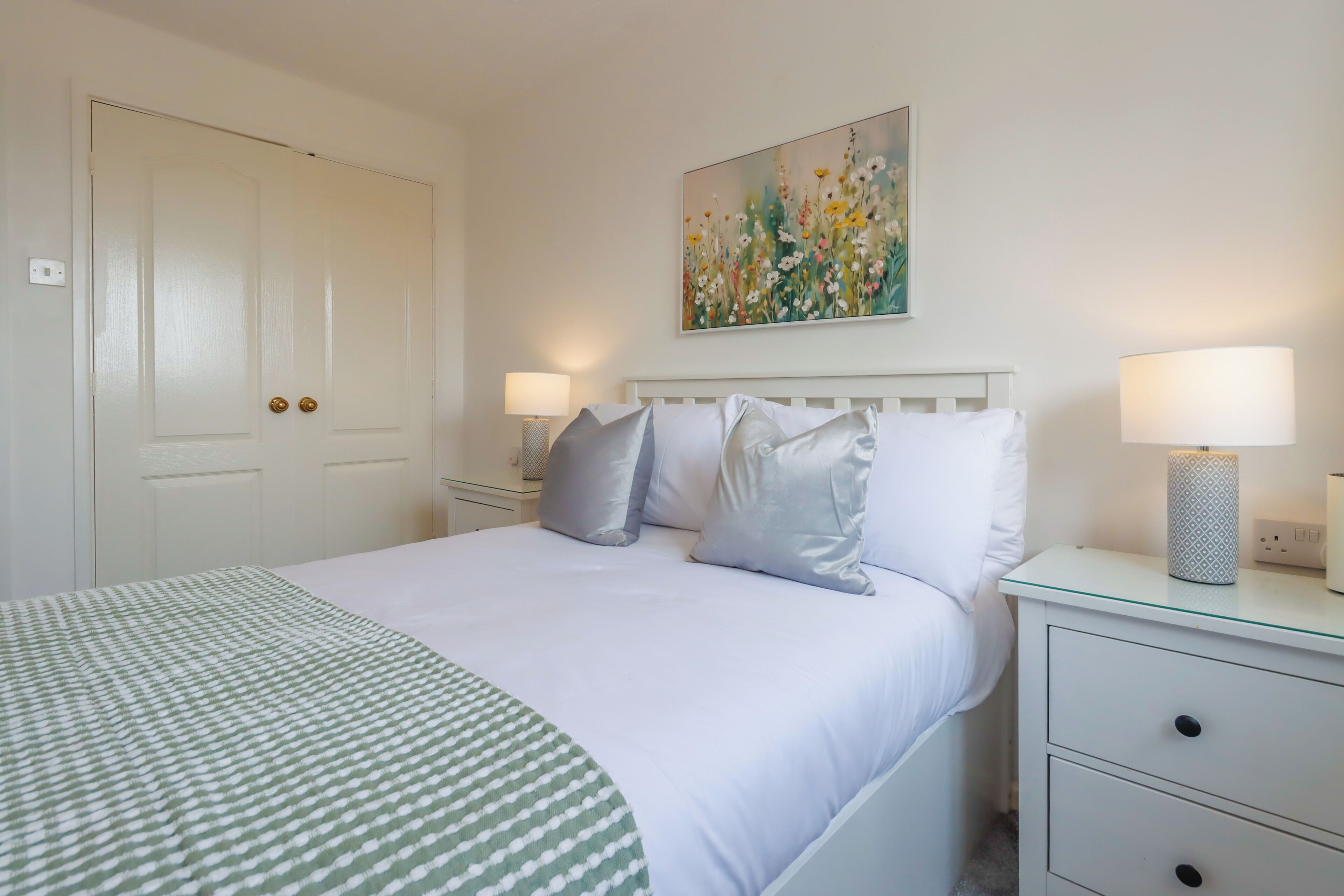 A neatly arranged bedroom with a bed, bedside tables, and a painting on the wall.