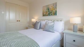 A neatly arranged bedroom with a bed, bedside tables, and a painting on the wall.