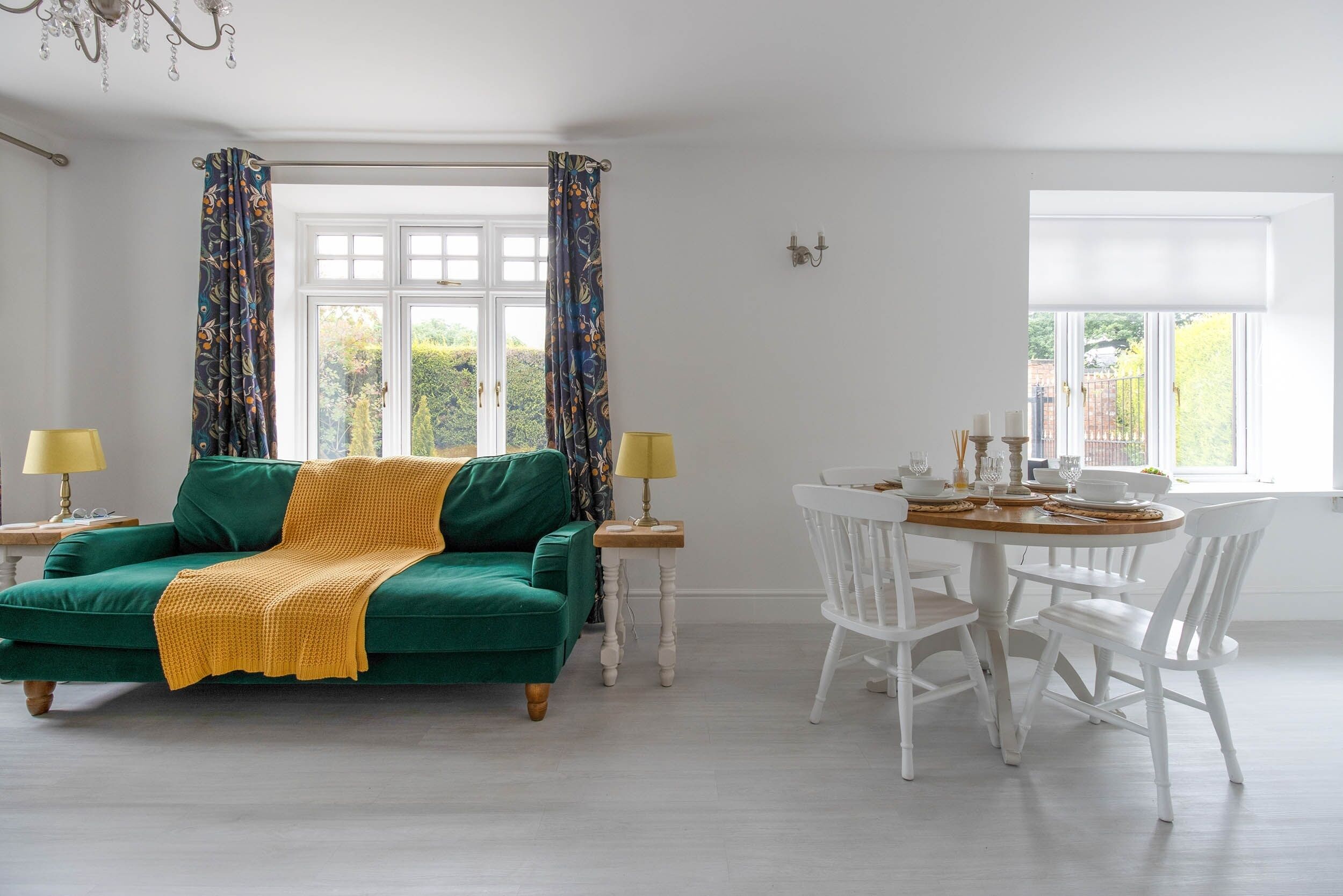 Ein Zimmer mit einem grünen Sofa, weißen Stühlen, einem Esstisch und einem Fenster mit Vorhängen.