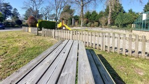 A wooden bench in a park with a wooden fence and trees in the background.