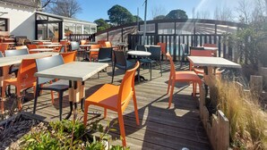 An outdoor patio with wooden decking, orange and black chairs, and tables.