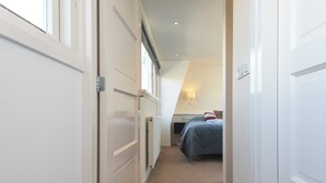 Un corridoio stretto che porta a una camera da letto con soffitto spiovente e termosifone.